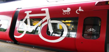 Côté latérale d'un train rouge avec marquage blanc de pictogrammes d'un vélo sur la totalité de la hauteur et d'une poussette et d’un fauteuil handicapé